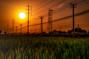 High voltage electric pole and transmission lines at sunset time with orange and red sky and clouds.