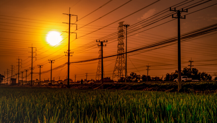 High voltage electric pole and transmission lines at sunset time with orange and red sky and clouds.
