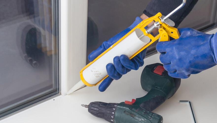 Homeowner sealing window with caulk indoors.