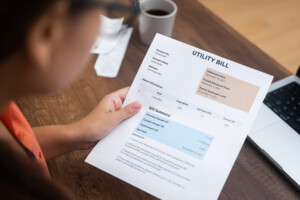 Woman reading her electric bill while sitting at home at wooden table with cup of coffee and open laptop