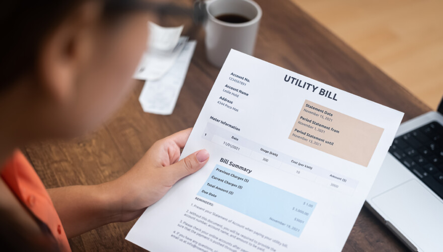 Woman reading her electric bill while sitting at home at wooden table with cup of coffee and open laptop