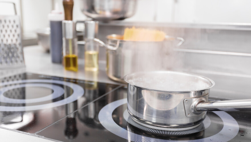 A pot of boiling water sits on an electric stove while steam rises, indicating boiling pasta.