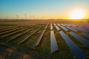 Solar panels and wind turbines in rural landscape at sunset.