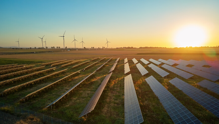 Solar panels and wind turbines in rural landscape at sunset.
