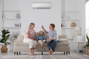 Family resting together on sofa at home. Man switching on air conditioner with remote control
