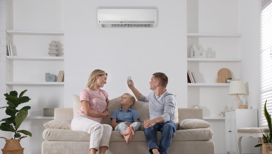Family resting together on sofa at home. Man switching on air conditioner with remote control