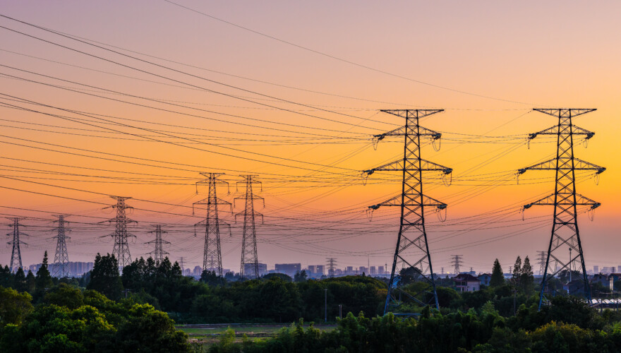 High voltage electricity pylons and transmission lines at sunset.