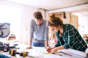 Man and woman worker examine blueprints while remodeling their home.