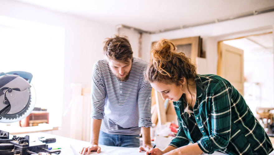Man and woman worker examine blueprints while remodeling their home.