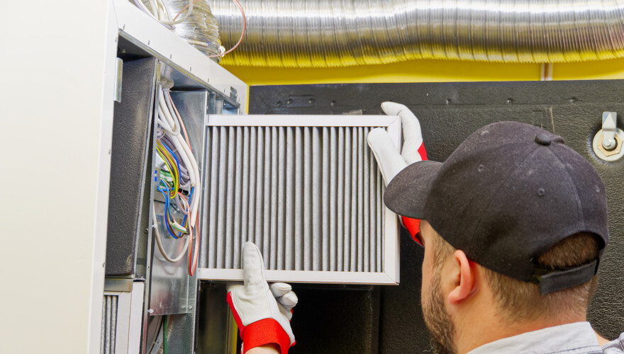 HVAC service technician changing dirty air filter in a central ventilation system.
