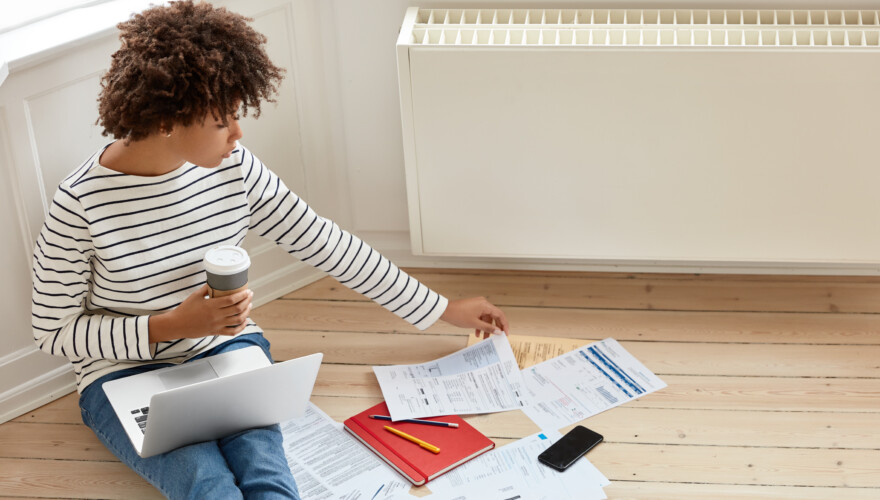 A woman sitting on the floor reading her monthly energy bills