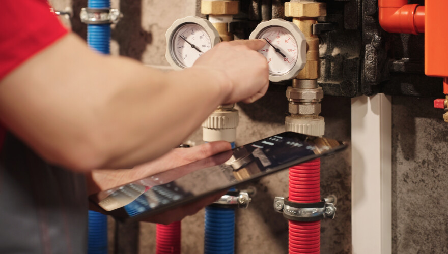Technician Checking Heating System Gauges Using Digital Tablet