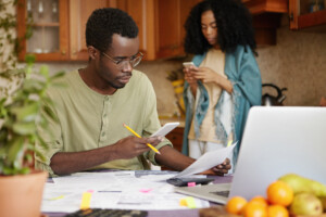 A dark-skinned male holding a mobile phone in one hand and piece of paper in other, comparing energy services